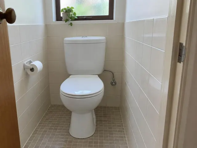 Clean white toilet in a small tiled bathroom with a window and toilet paper holder in Bonnyrigg